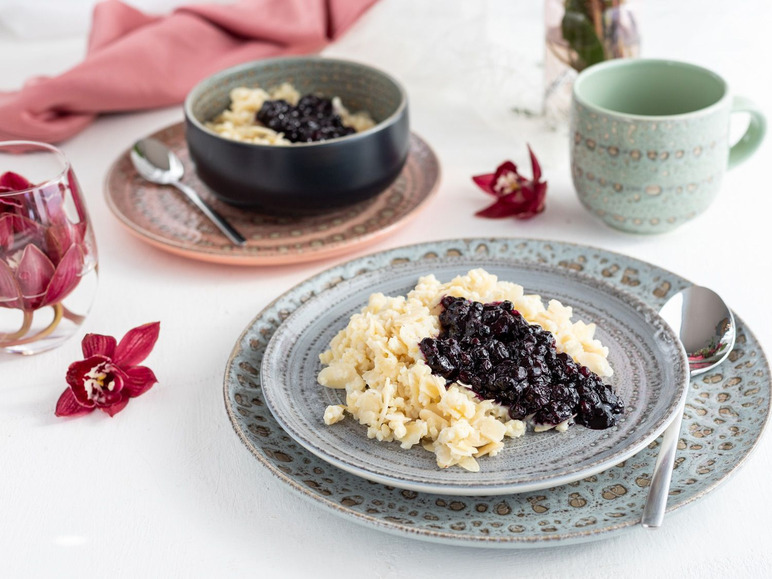 Zwei Schüsseln mit Milchreis und Blaubeeren, serviert auf einem dekorativen Teller.