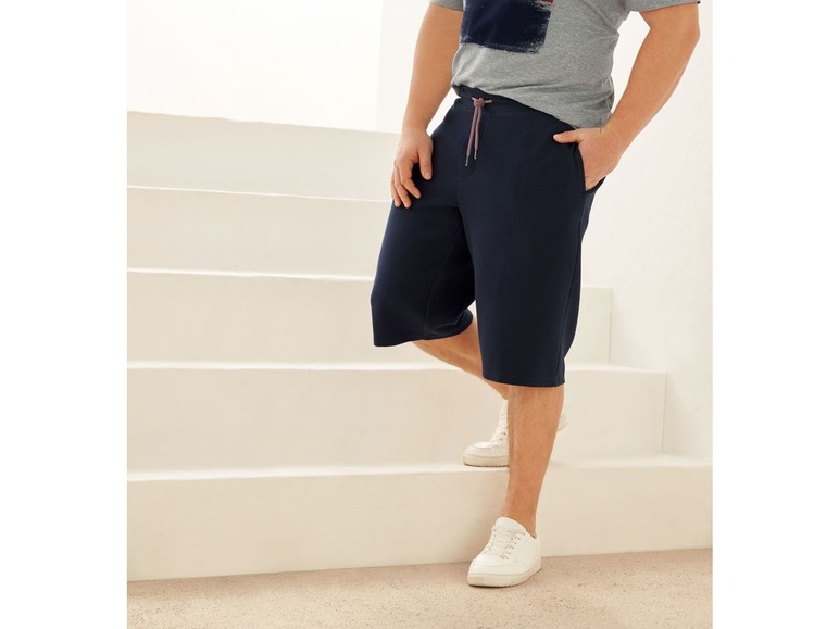 Mann in blauen Shorts und weißen Sneakers.