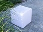 Ein weißer Kubussitz auf einer gepflasterten Terrasse.