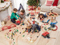 Kinder spielen mit einer großen Holzeisenbahn mit Brücke, Tunneln und verschiedenen Zubehörteilen.