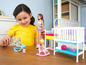 Ein Mädchen spielt mit Barbie Puppen und Zubehör, darunter ein Babybett und ein Schaukelstuhl.