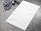Ein weißer Badeteppich mit wellenförmiger Textur auf einem grauen Fliesenboden.