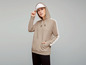 Eine Frau trägt einen beigefarbenen Hoodie mit weißen Akzenten und einer weißen Baseballkappe.