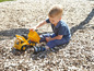 Ein Junge spielt mit einem gelben Spielzeug-LKW auf einem Spielplatz.
