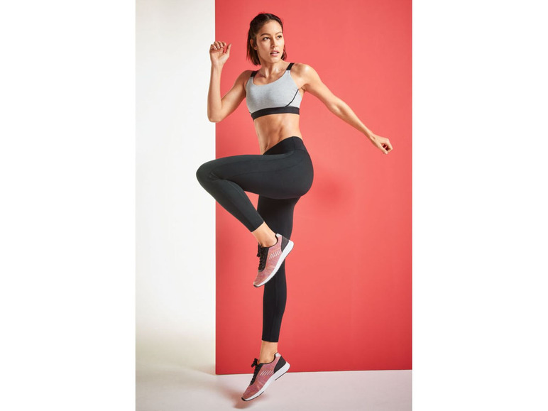 Frau in Sport-BH, Leggings und Sneakers in sportlicher Pose.