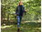 Eine Frau wandert mit Wanderstöcken und einer schwarzen Jacke durch einen Wald.