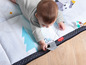 Ein Baby auf einer Spielmatte von Tiny Love mit einem Baum und Tieren.