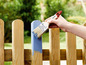 Eine Hand streicht einen Holzzaun mit einem Parkside Pinsel an.