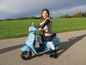 Ein Mädchen fährt auf einem blauen Vespa-ähnlichen Elektro-Roller.
