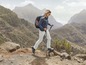 Eine Frau wandert mit Stöcken und Rucksack durch eine bergige Landschaft.