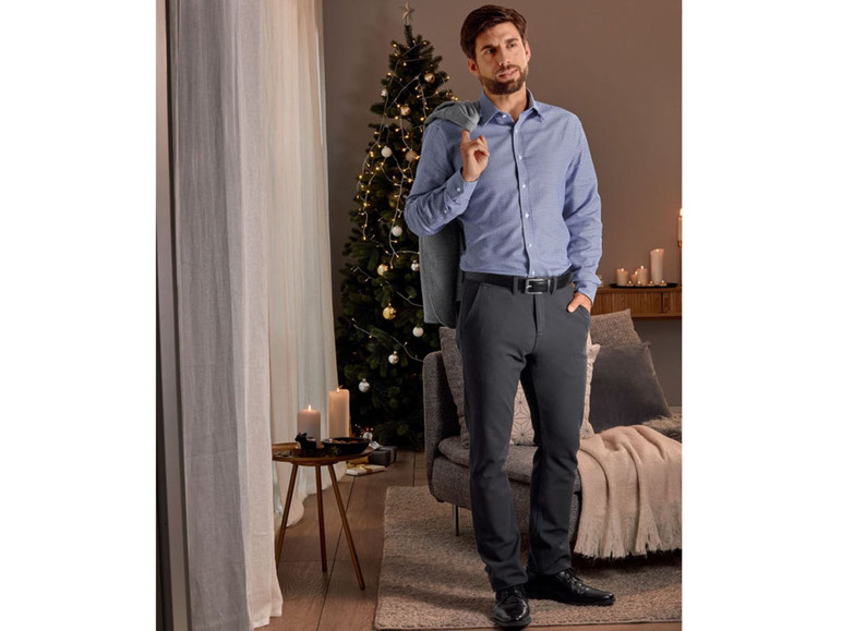 Mann in gestreiftem Hemd und schwarzen Hosen vor weihnachtlichem Hintergrund.