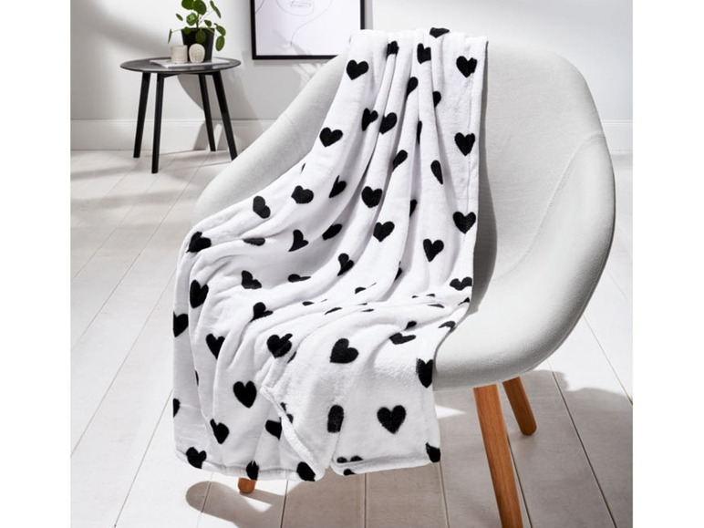 Eine weiße Fleece-Decke mit schwarzen Herzen auf einem Stuhl.