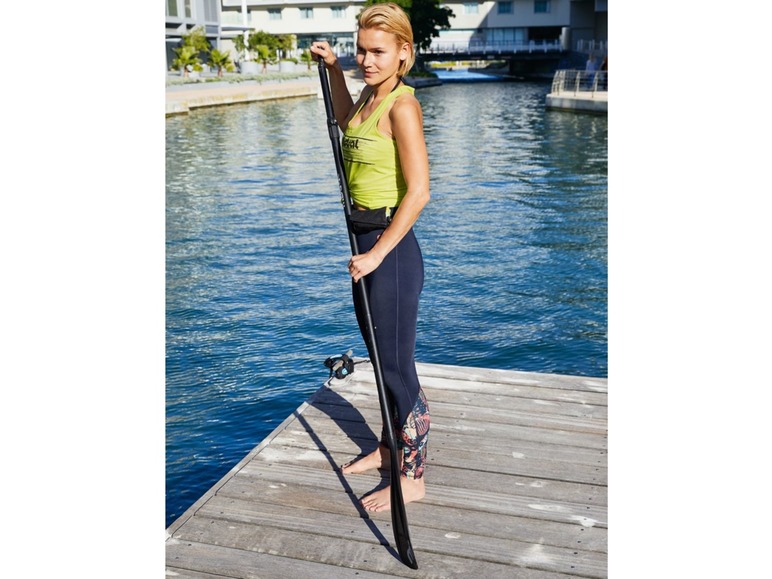 Eine Frau mit einem Paddleboard-Paddel auf einem Steg.