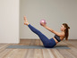 Eine Frau macht Pilates-Übungen mit einem rosa Ball auf einer Matte.