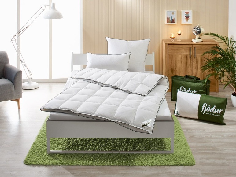 Eine weiße Bettdecke und ein Kissen von Fjodor auf einem Bett mit einem grünen Teppich.