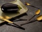 Eine Aubergine, ein Messer und Besteck mit goldenen und schwarzen Griffen.