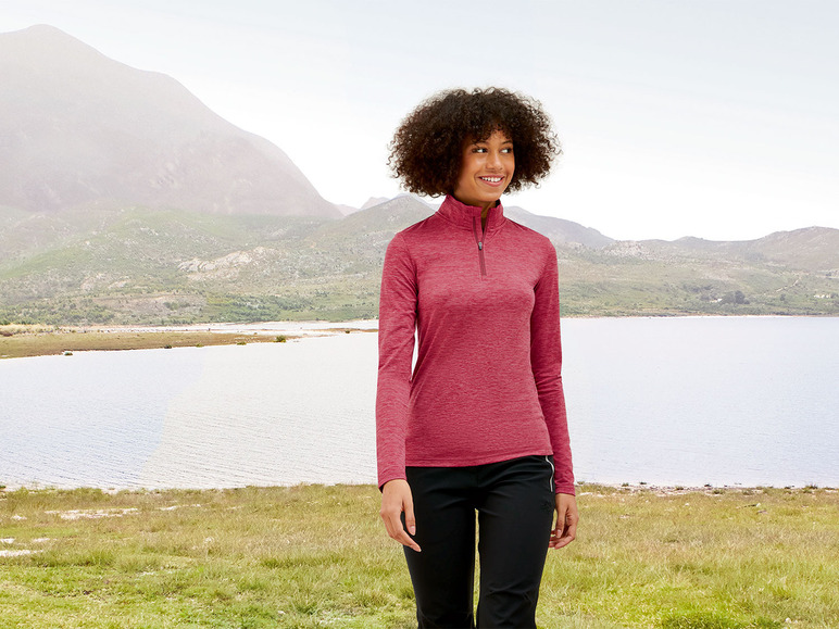 Eine Frau in einem roten Oberteil und schwarzen Hosen, die durch eine Landschaft mit einem See geht.