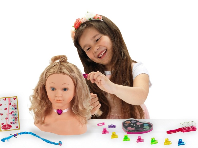 Ein Mädchen spielt mit einem Puppenkopf, Haarschmuck und Make-up.