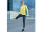 Eine Frau trägt Sportbekleidung, darunter ein neon-gelbes Oberteil und schwarze Leggings mit weißen Details.
