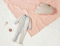 Ein gestreifter Baby-Strampler, ein rosa Wolkenkissen und Spielzeug auf einer weißen Oberfläche.