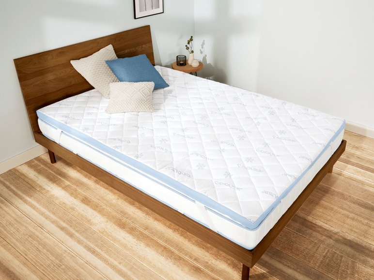 Ein Coolers® Matratzenauflage auf einem Holzbettgestell.
