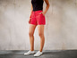 Eine Frau in roten Shorts und weißen Sneakern.