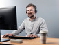 Ein Mann mit Headset arbeitet an einem Computer mit einer Tasse Kaffee.