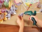 Eine Hand verwendet eine Parkside Heißklebepistole zum Befestigen von Papierblumen.