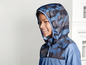 Ein Junge trägt eine blaue Windjacke mit Camouflage-Muster.