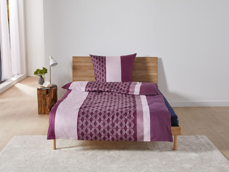 Ein Bett mit einem violetten Bettbezug mit geometrischem Muster.