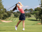 Eine Frau in Golfkleidung schwingt einen Golfschläger auf einem Golfplatz.