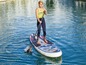 Eine Frau steht mit einem Paddleboard und Paddel auf dem Wasser.