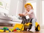 Ein Mädchen spielt mit einem gelben Spielzeugtraktor und Bausteinen.