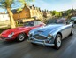 Ein blauer Austin-Healey und ein roter Jaguar fahren durch ein englisches Dorf.