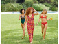 Drei Frauen in Badebekleidung und einem langen Sommerkleid gehen über eine Wiese.