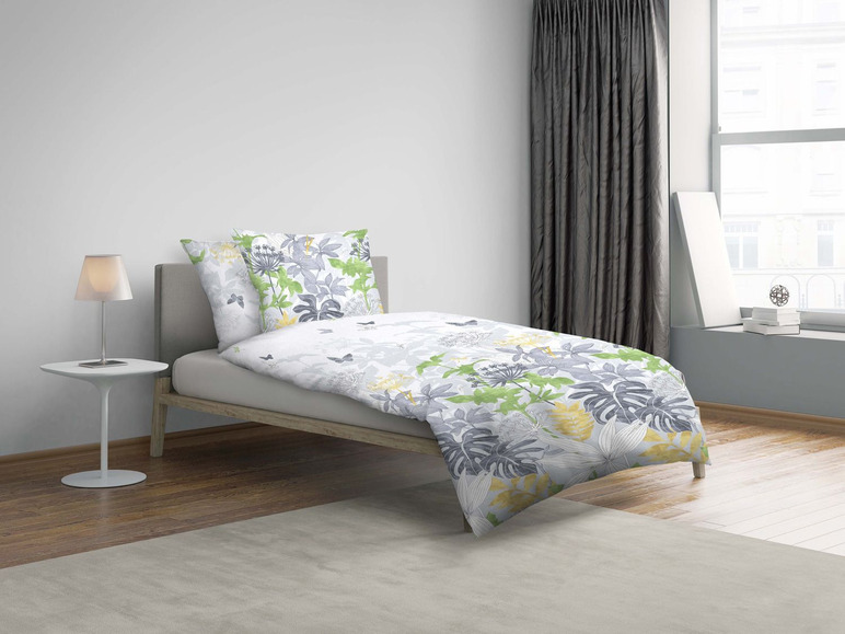 Ein Bett mit einem weißen Bettbezug mit grünen und grauen tropischen Blättern.