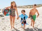 Kinder am Strand mit einem Paw Patrol aufblasbaren Ball, einem Mickey Mouse Handtuch und Badebekleidung.