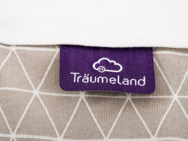 Ein lilafarbenes Etikett mit dem Schriftzug 'Träumeland' auf einem beigefarbenen Textilhintergrund.