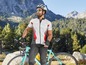Ein Radfahrer in einem weißen Trikot und einem Helm fährt ein blaues Rennrad in einer Berglandschaft.