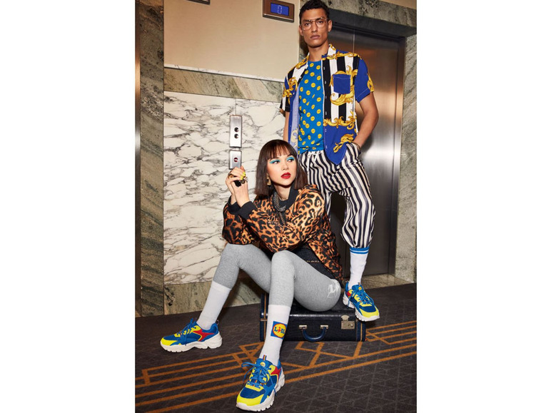 Zwei Personen posieren in einem Aufzug, gekleidet in leuchtenden Farben und Sneakers.