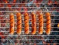 Sechs Würstchen auf einem Grillrost.