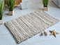Beige Badematte mit grober Textur und dekorativen Muscheln.