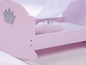 Ein rosa Holz-Puppenbett mit einer Krone und einem Kissen mit Blumenmuster.