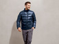 Ein Mann trägt eine dunkelblaue Jacke und graue Hose.