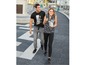 Ein Mann und eine Frau gehen auf der Straße, er trägt ein schwarzes T-Shirt und graue Hosen, sie ein gemustertes Oberteil und schwarze Leggings.