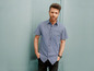Mann in einem karierten Hemd posiert vor einer blauen Wand.