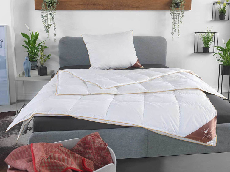 Eine weiße Bettdecke von Halssen mit beigefarbener Einfassung auf einem grauen Bett.