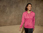 Eine Frau trägt eine rosafarbene Kapuzenjacke und schwarze Trainingshose.