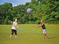 Zwei Personen spielen mit einem blauen Ball und Schaumstoffstöcken auf dem Rasen.