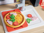 Eine Spielzeugküche mit Pizza und Belägen wie Schinken, Tomaten und Basilikum.